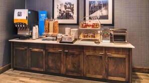 A breakfast bar with a coffee machine, a juice dispenser, and various food items.