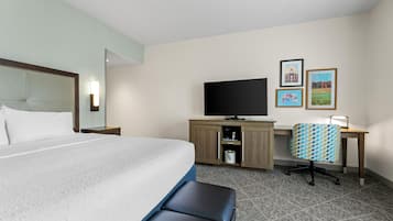 Quarto de hotel com cama, escrivaninha, televisão e obras de arte na parede.