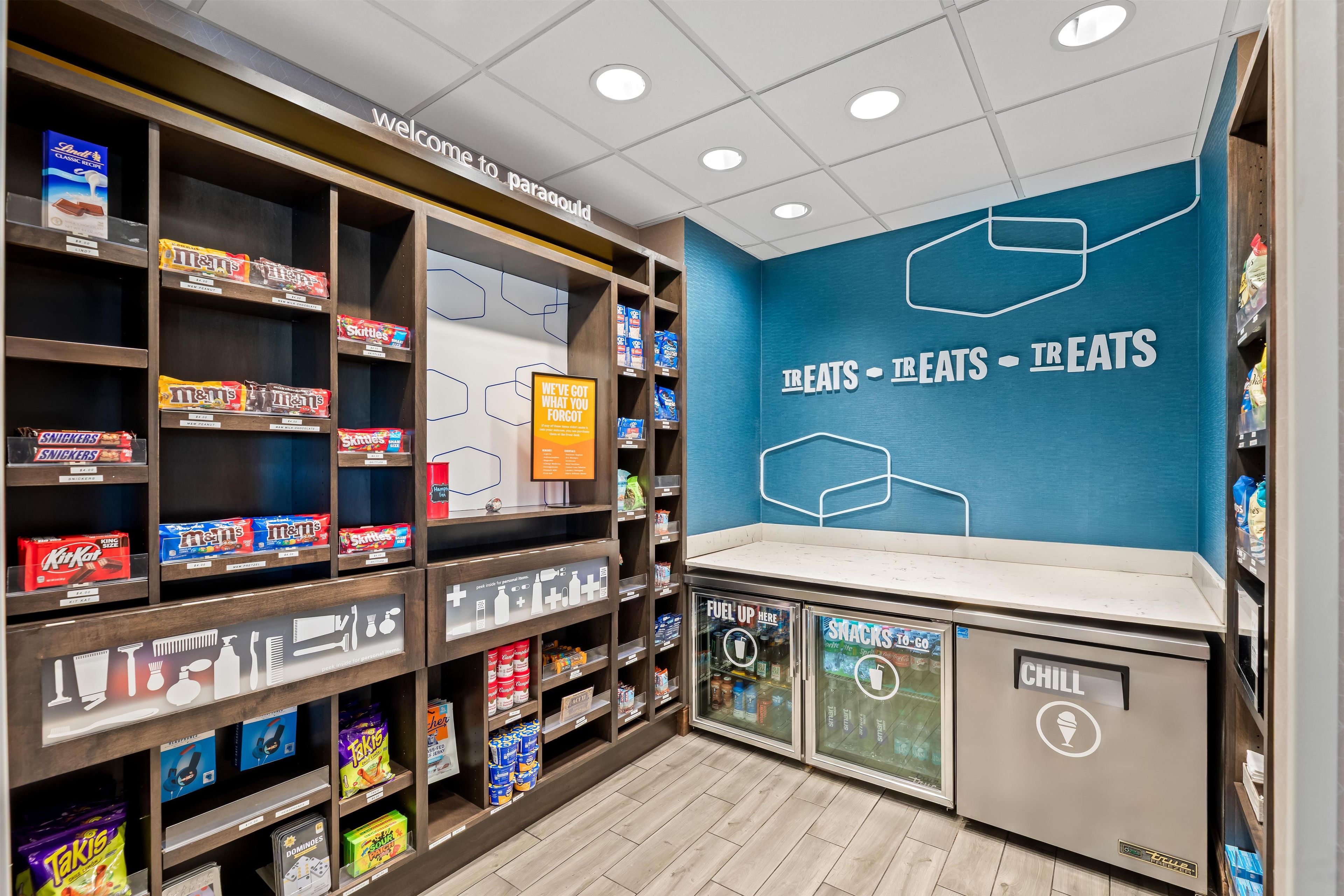 A snack and beverage section with shelves stocked with various brands and a wall with the text 'TREATS - TREATS - TREATS'.