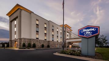 A Hampton Inn by Hilton hotel with a stone facade, multiple windows, and an American flag.
