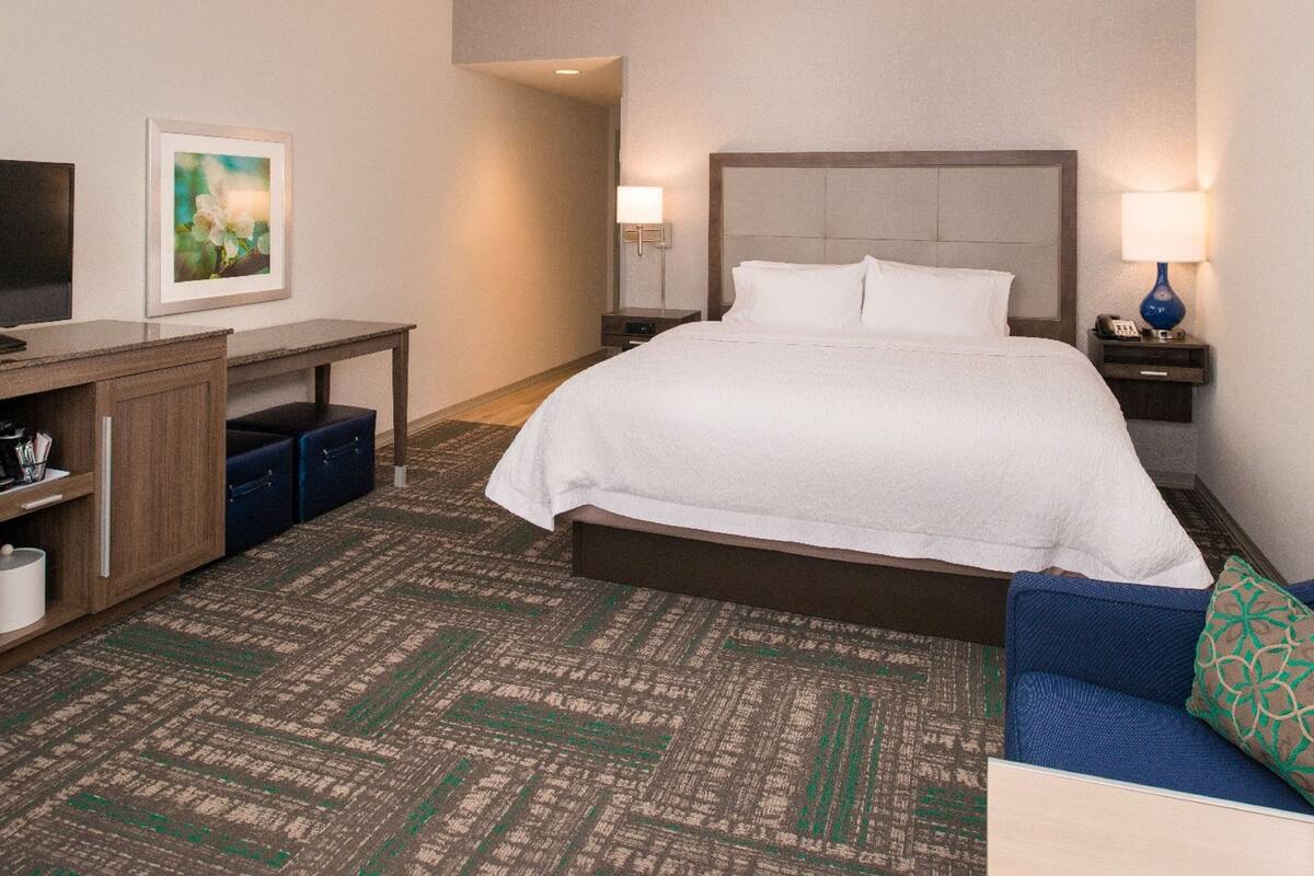 A hotel room with a bed, a desk, a chair, a TV, and a lamp.