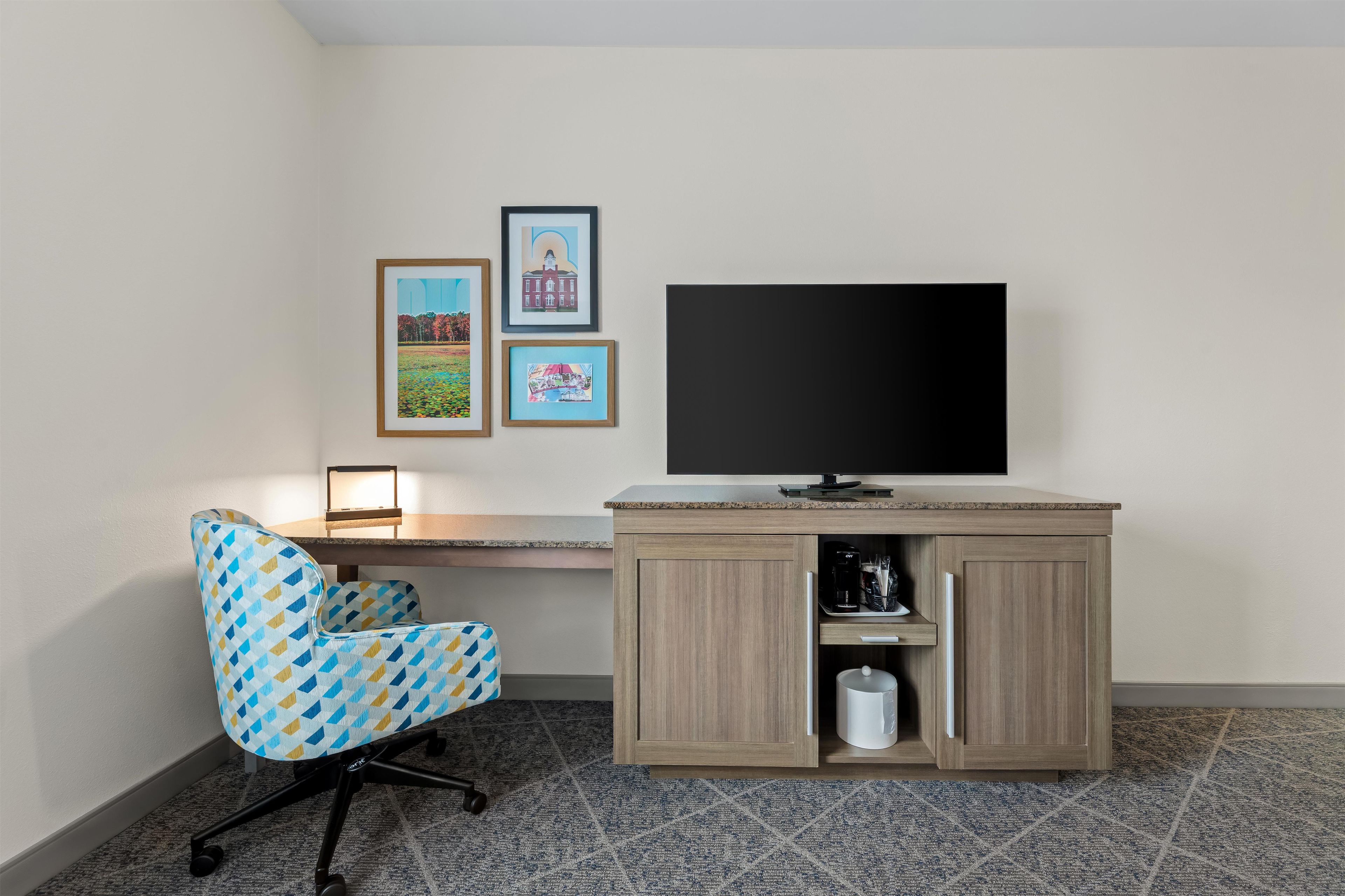Ein Zimmer mit Schreibtisch, Stuhl, Fernseher und drei gerahmten Bildern an der Wand.