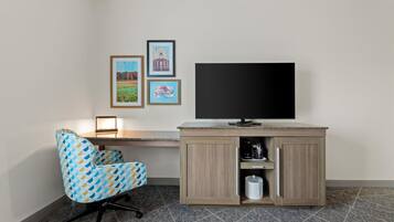Ein Zimmer mit Schreibtisch, Stuhl, Fernseher und drei gerahmten Bildern an der Wand.