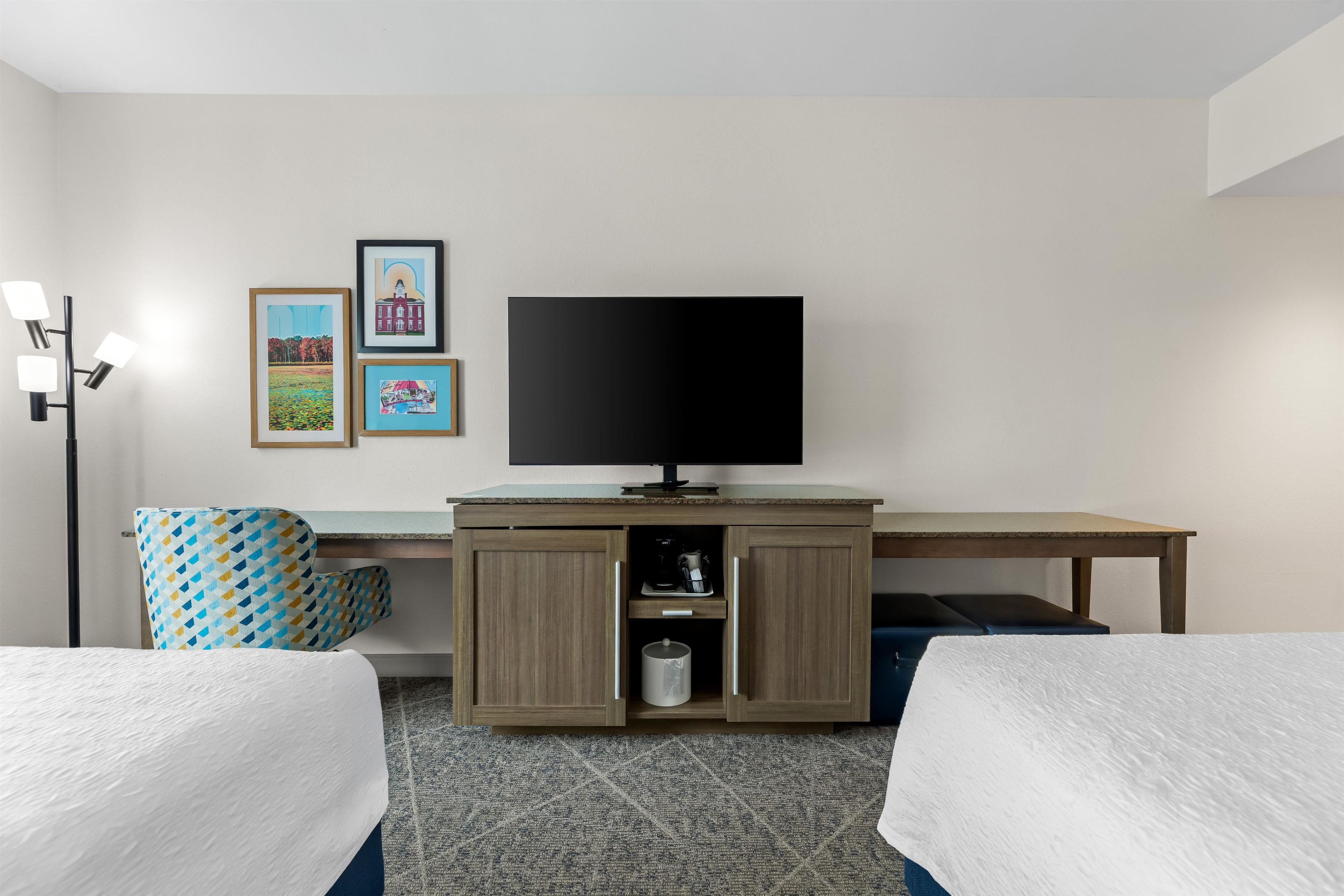 A hotel room with two beds, a desk with a television, and wall-mounted artwork.