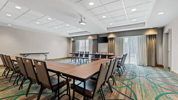 Un salón de conferencias con una larga mesa, sillas, un proyector y un amplio ventanal con cortinas.