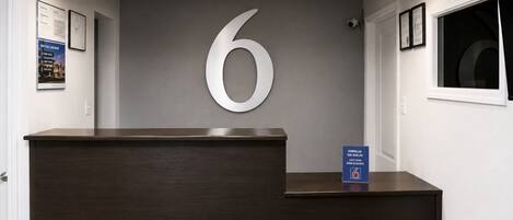 A reception desk with a large number '6' sign, a framed certificate, and a blue informational sign.
