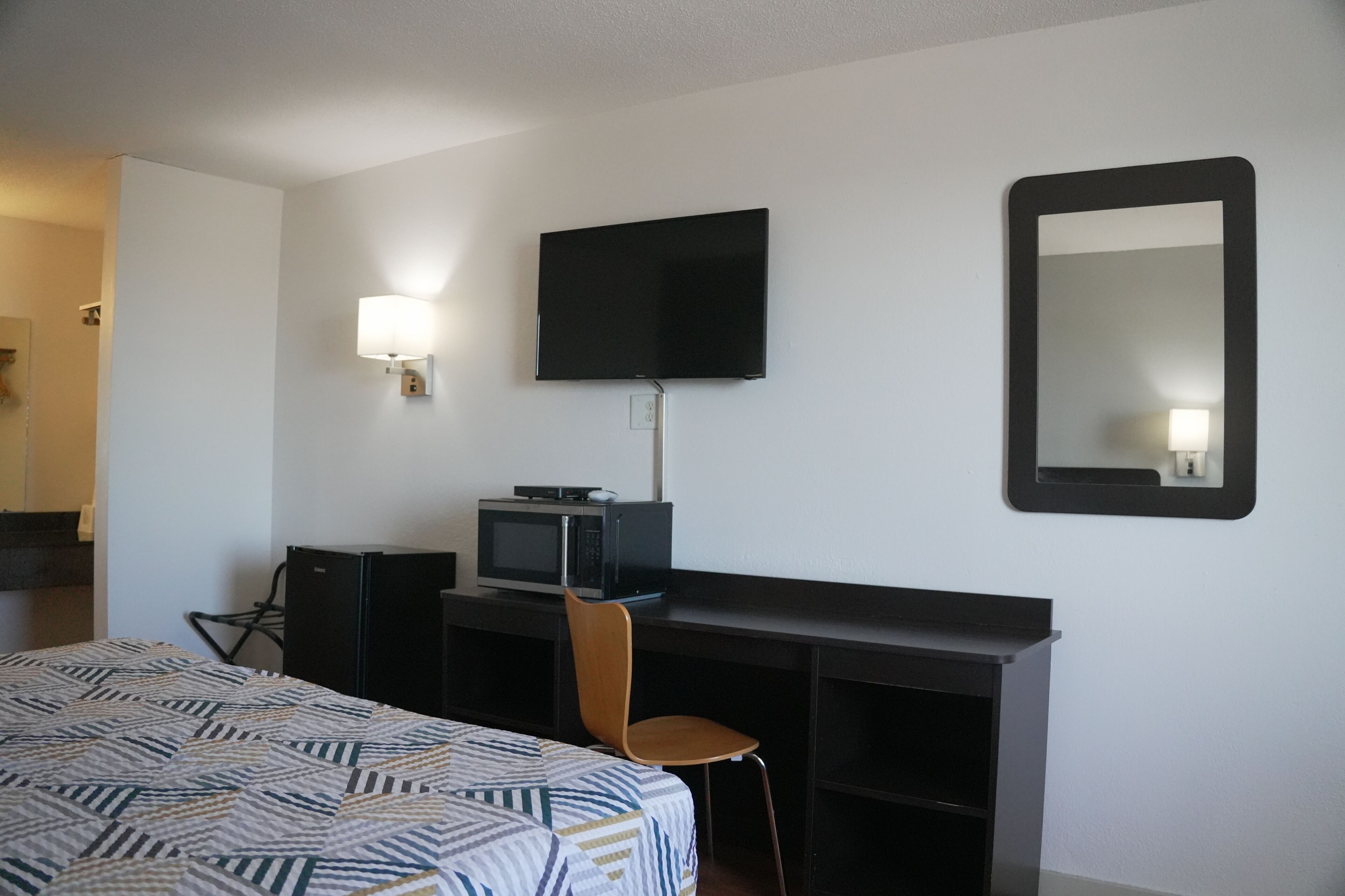 A hotel room with a bed, a desk with a computer, a television, a chair, and a mirror.