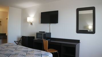 A hotel room with a bed, a desk with a computer, a television, a chair, and a mirror.