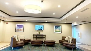 Een ruime lobby met een grote, moderne kroonluchter, drie bruine leren banken, een flatscreen-tv en kunstwerken in lijsten aan de wanden.