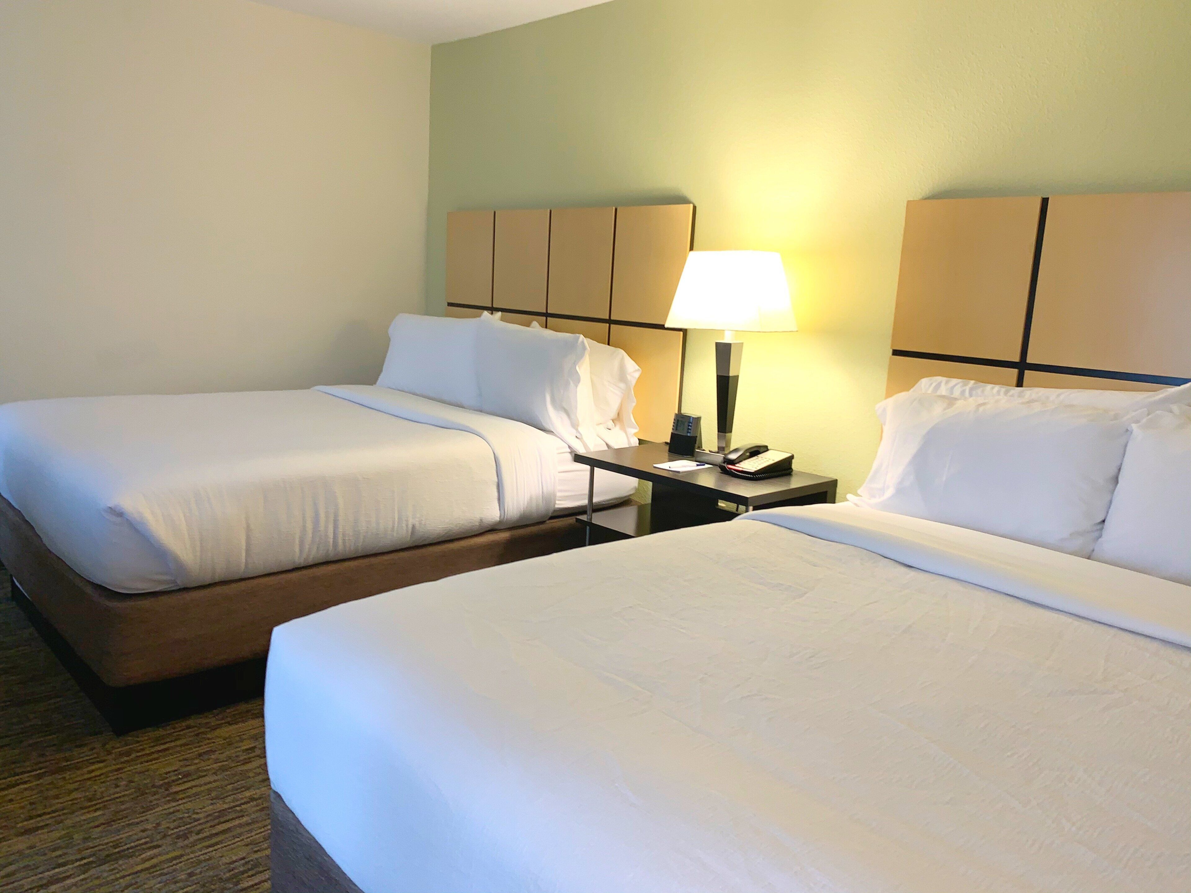 A hotel room with two beds, a nightstand with a lamp, and a telephone.