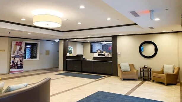 Een moderne hotellobby met een receptiebalie, een zithoek en een grote spiegel aan de muur.