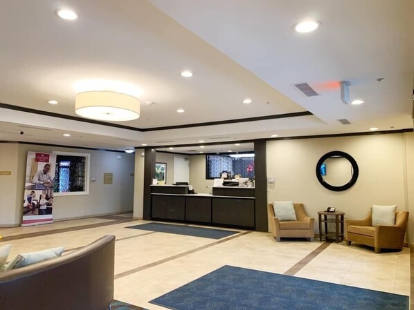 Un hall d’hôtel moderne avec un comptoir d’accueil, un espace salon et un grand miroir mural.