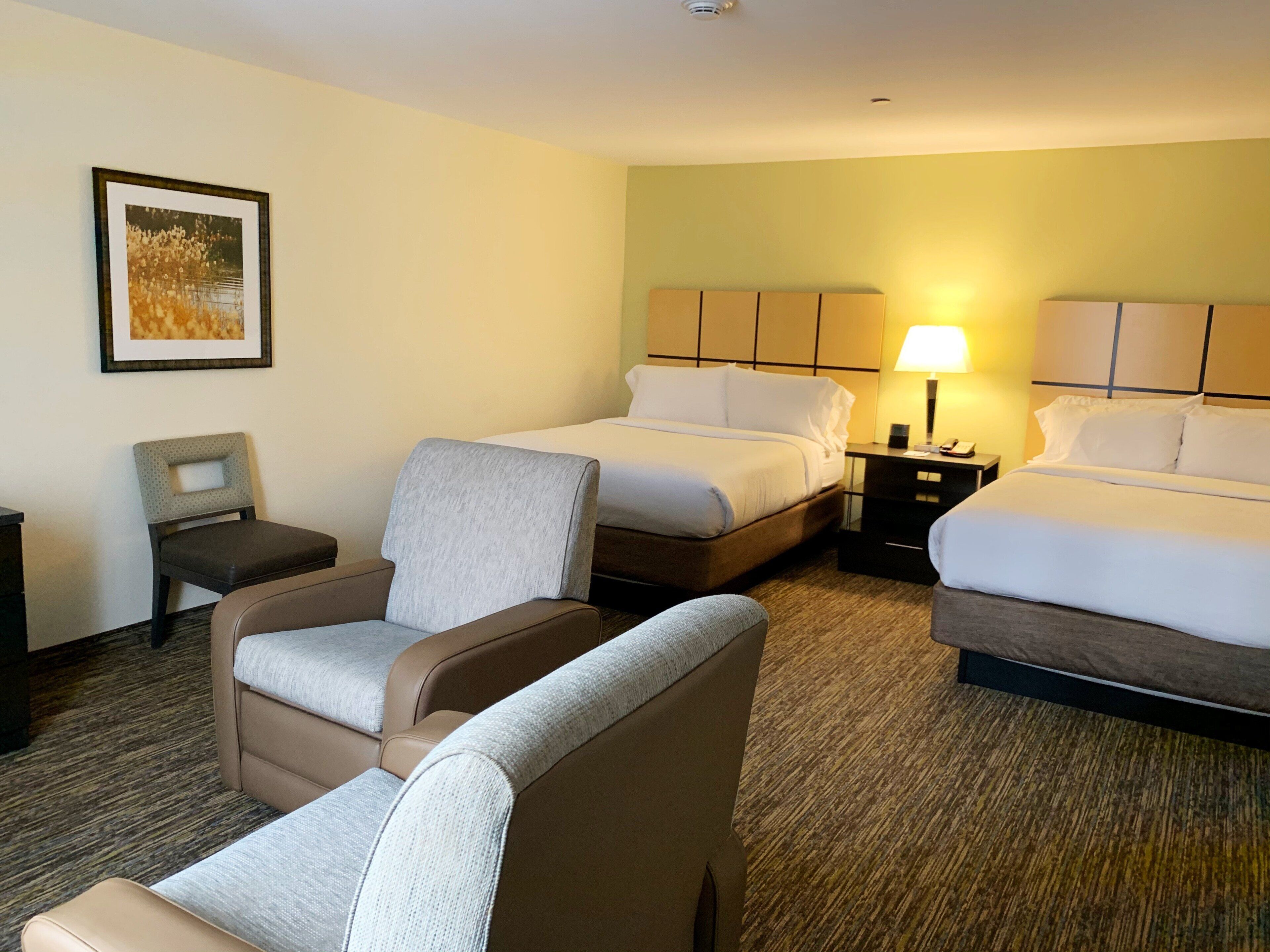 Een hotelkamer met twee bedden, een stoel, een nachtkastje en een lamp.