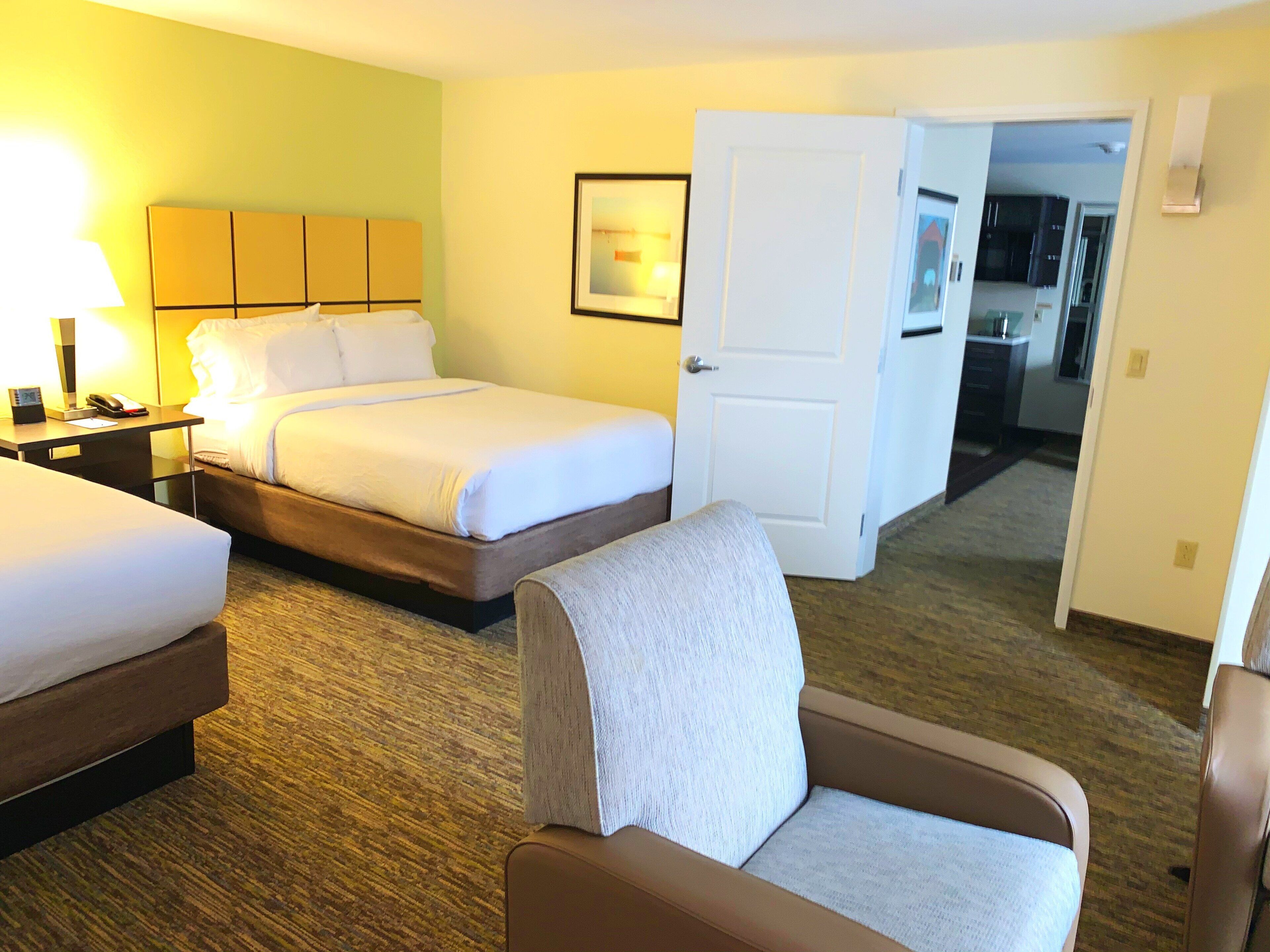 A hotel room with a bed, a chair, a desk with a lamp, and a door leading to a bathroom.