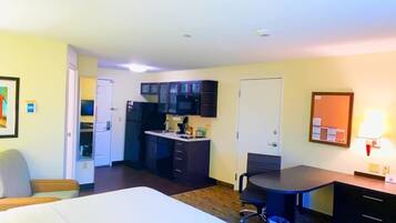 Una habitación de hotel con cama, escritorio, silla, kitchenette pequeño y puerta.