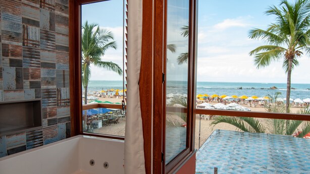 Un bagno con una vasca, una finestra vista spiaggia e pavimento piastrellato.