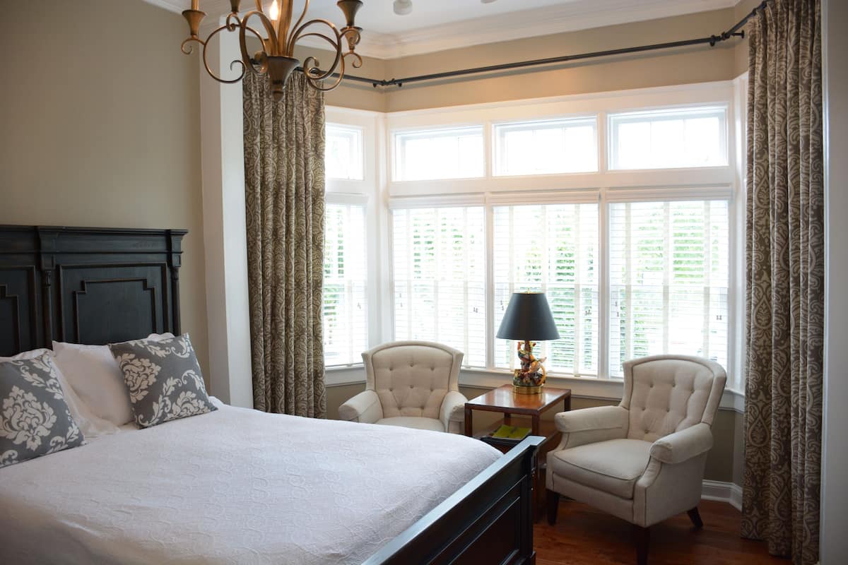 A bedroom with a large bed, two armchairs, a small table, and a window with curtains.