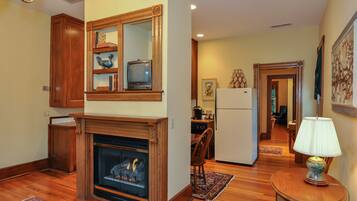 A living room with a fireplace, wooden cabinets, a television, and a kitchen area in the background.