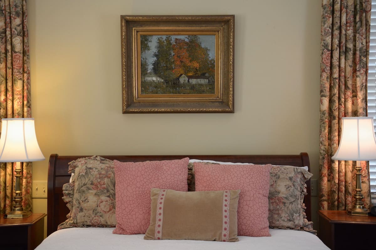 A neatly made bed with floral-patterned pillows and a framed painting above it.