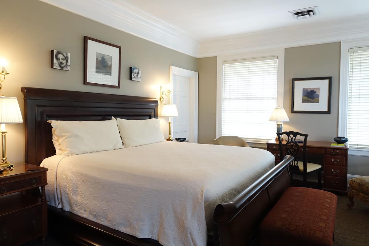 A neatly arranged bedroom with a large bed, bedside tables, a desk, and a chair.