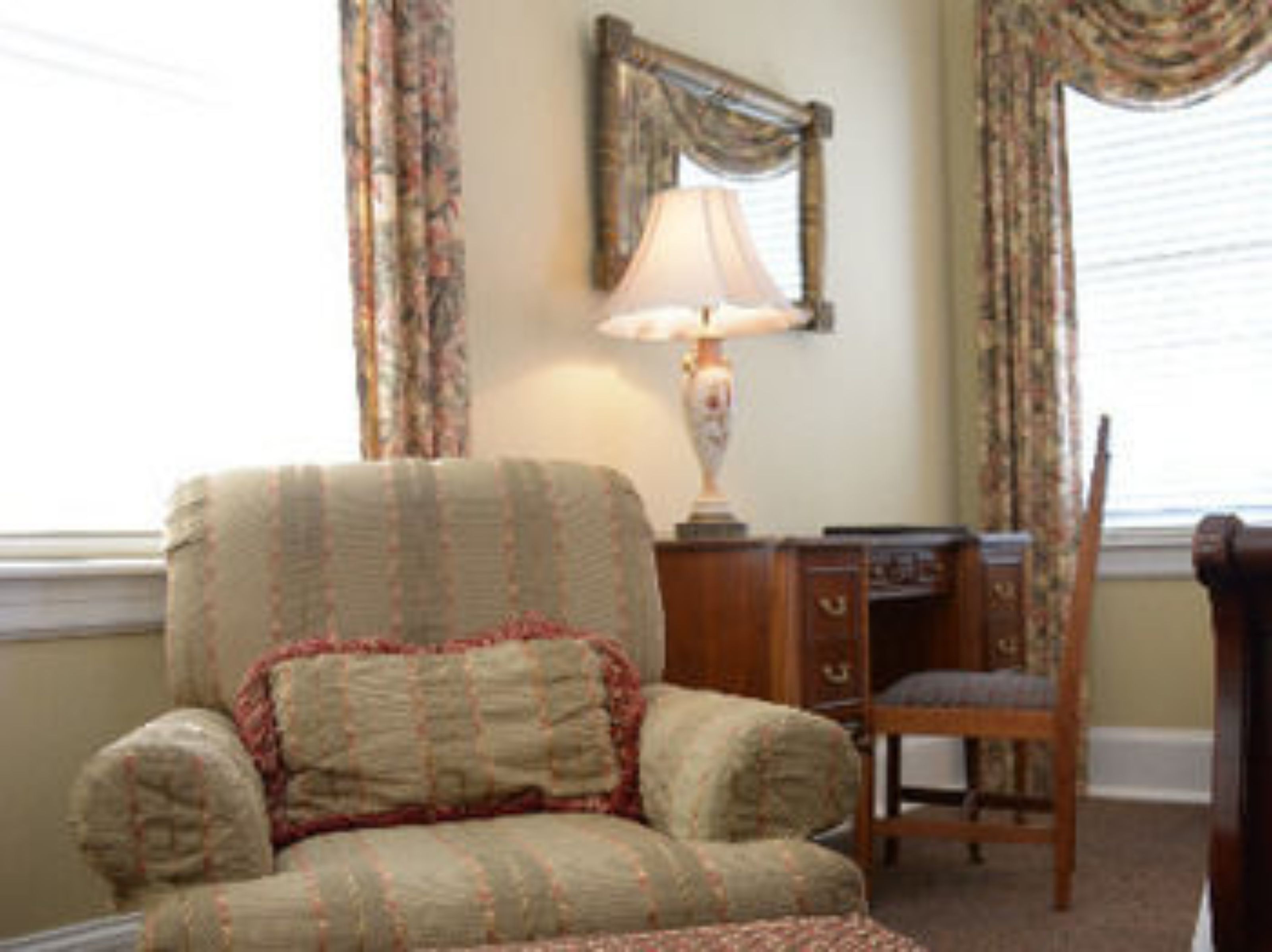 A room with a patterned armchair, a wooden desk, and a lamp.