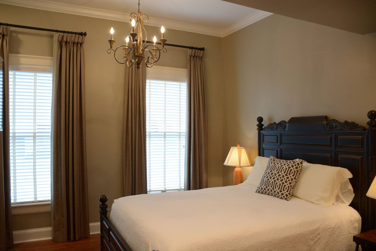 A bedroom with a large bed, a chandelier, and a nightstand with a lamp.