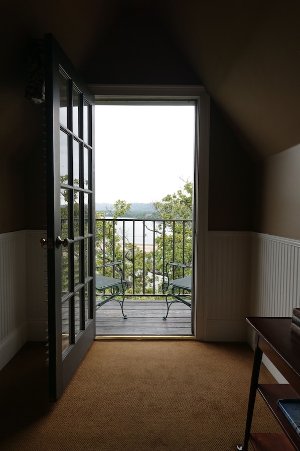 Quarto com uma grande porta de correr de vidro que dá para uma varanda com vista para um corpo de água e montanhas.