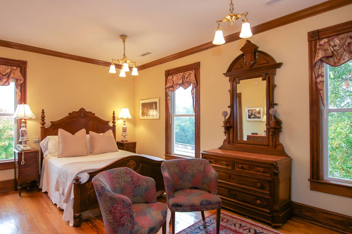A bedroom with a wooden bed, two upholstered chairs, a dresser, and a large mirror.