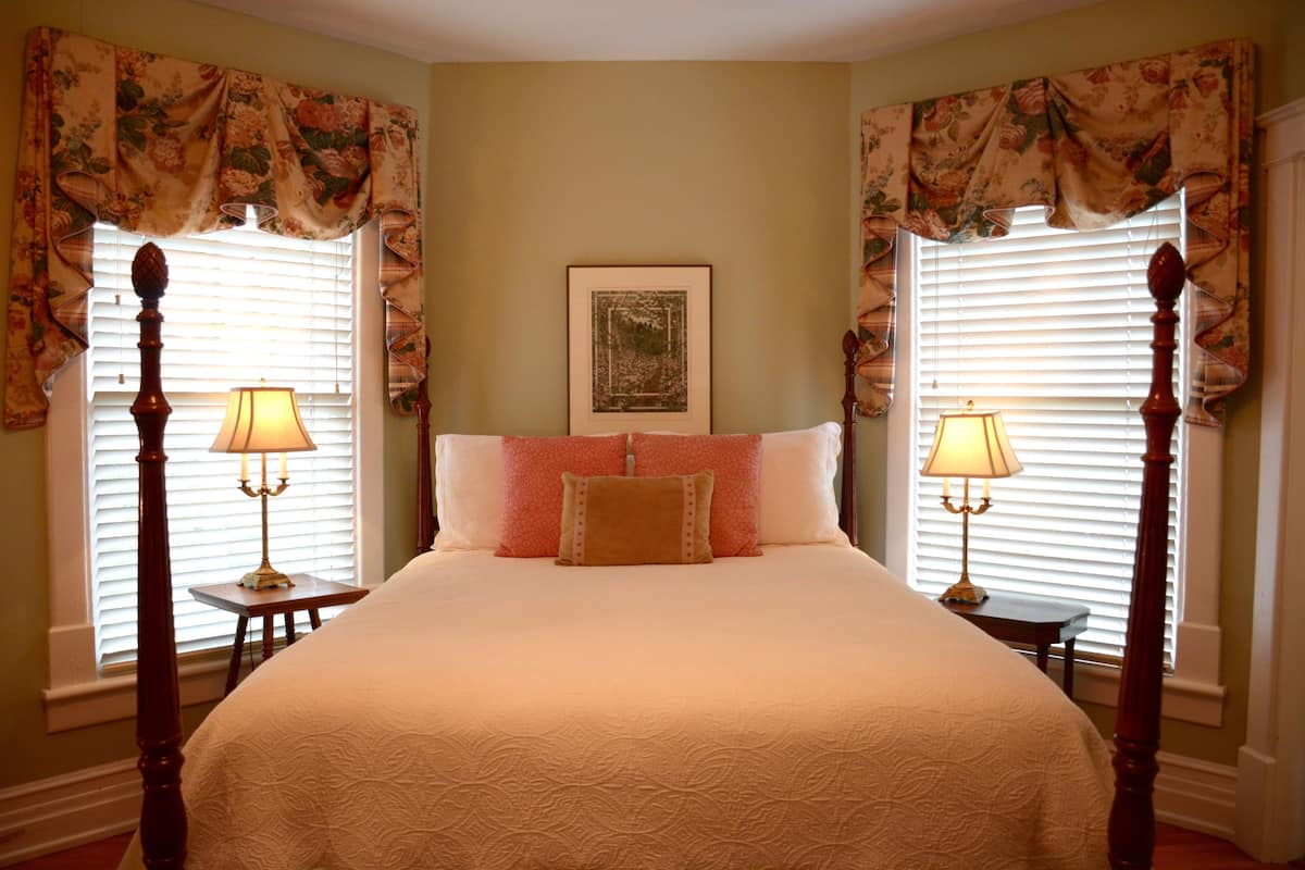 A bedroom with a large bed, two bedside tables with lamps, floral curtains, and a framed picture on the wall.