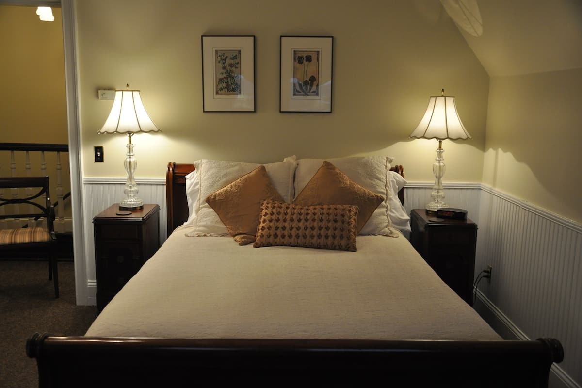 A neatly made bed with two lamps on either side, a chair, and two framed pictures on the wall.