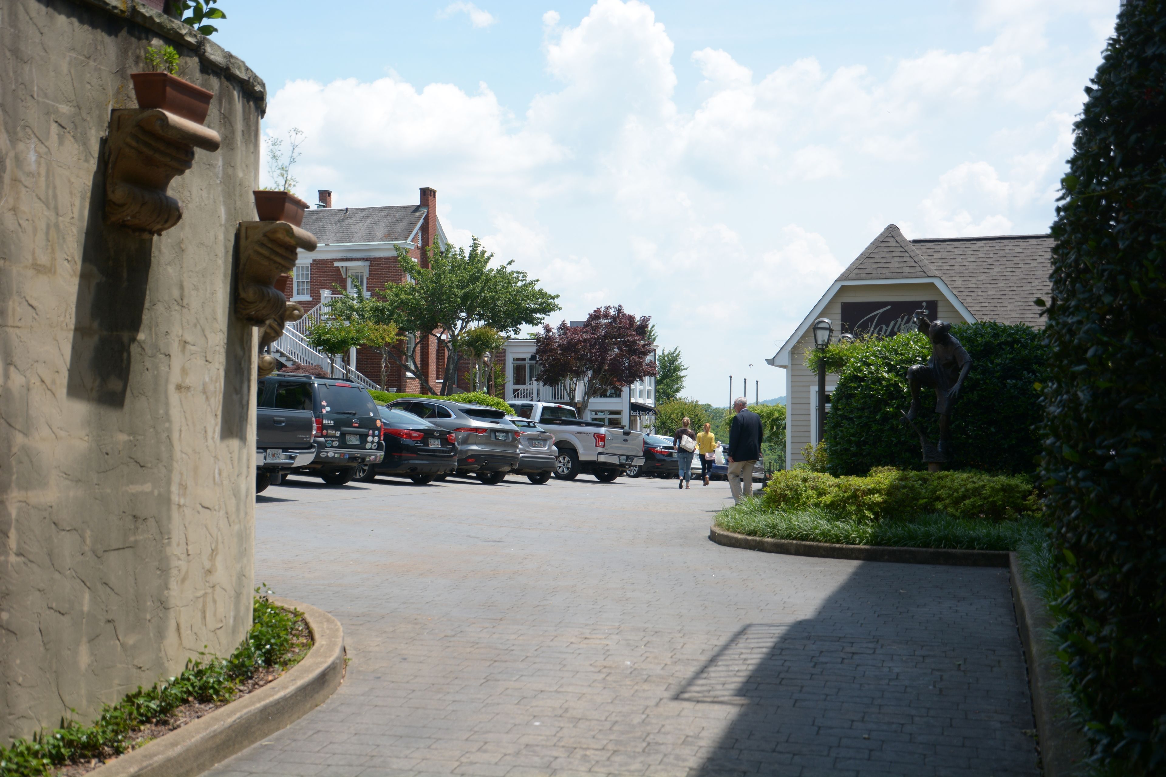 A paved street with parked cars, a stone wall with planters, and a building with a gabled roof.