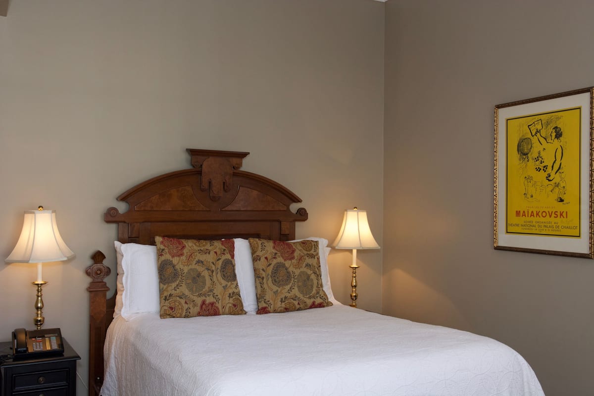A neatly made bed with a wooden headboard, two bedside lamps, and a framed poster on the wall.