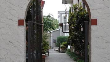 An arched entrance with a metal gate, leading to a paved pathway lined with potted plants and a bench.