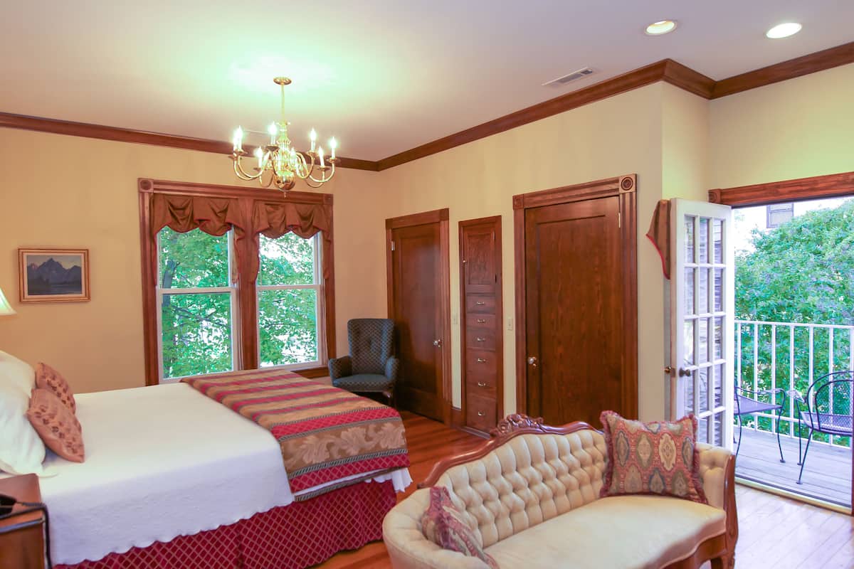 A bedroom with two beds, a chandelier, a chair, and a balcony with a view of greenery.