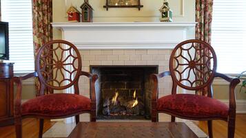 A fireplace with two ornate chairs facing it, a mantelpiece with decorative items, and a television on the left.
