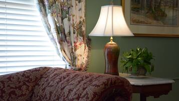 A bedroom with a bed, a lamp, a plant, and a painting on the wall.