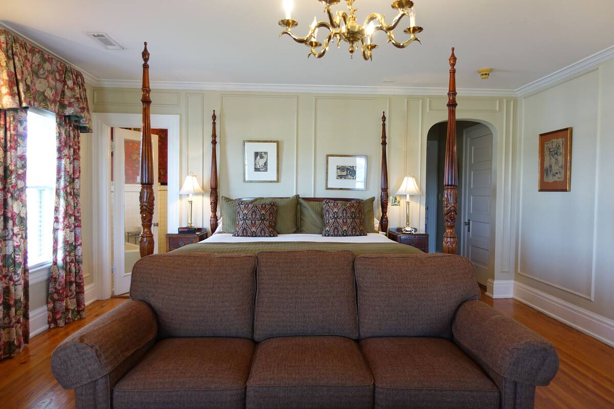 A bedroom with a four-poster bed, a large sofa, and a chandelier.
