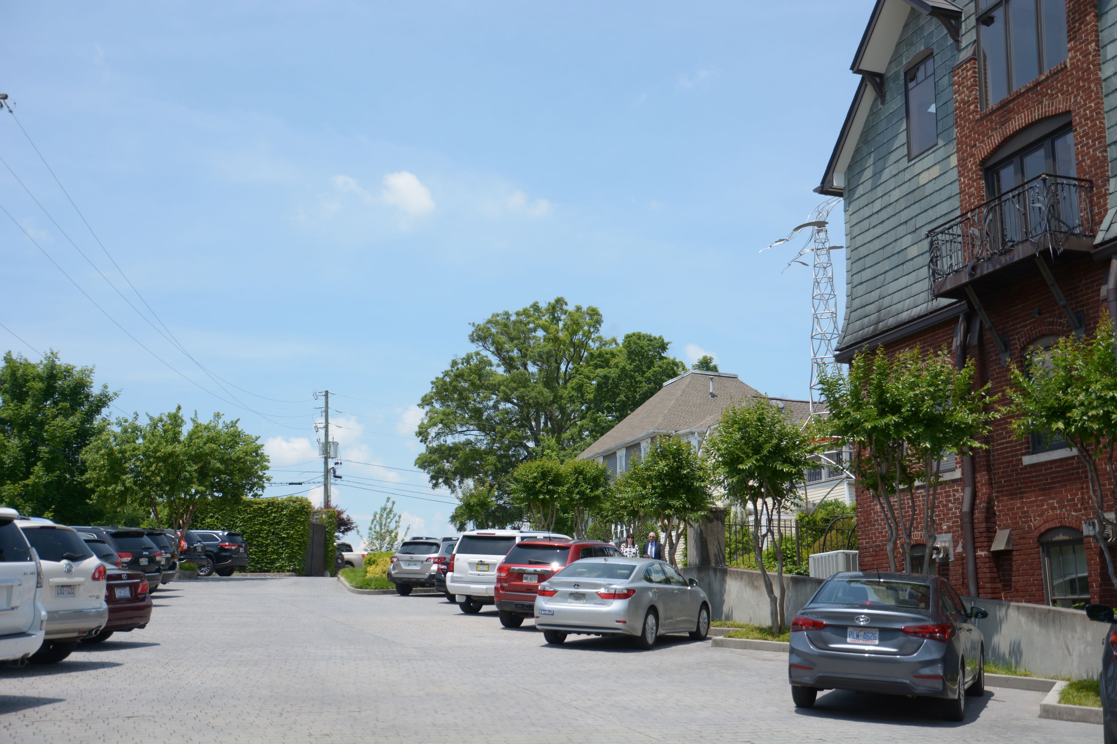 A residential street with parked cars, houses, and a clear sky.
