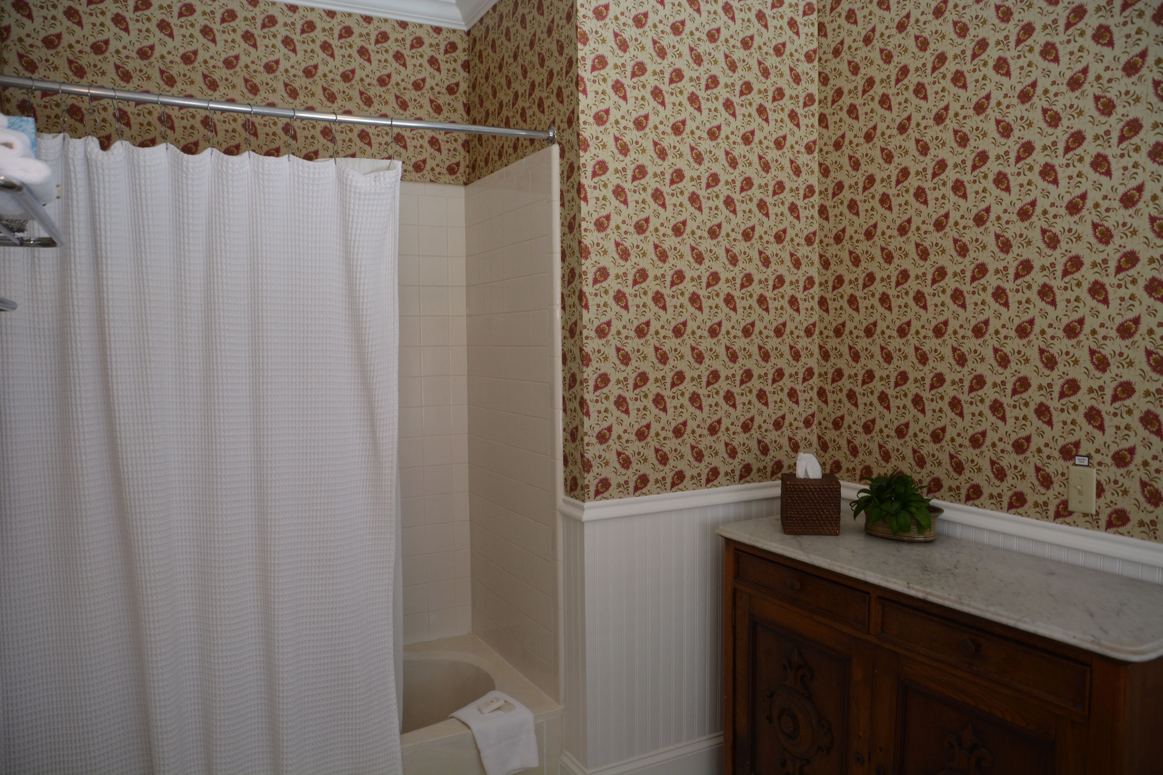 A bathroom with a shower curtain, a bathtub, a vanity with a mirror, and patterned wallpaper.