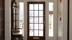 Um corredor com porta de madeira, lustre e tapete estampado.