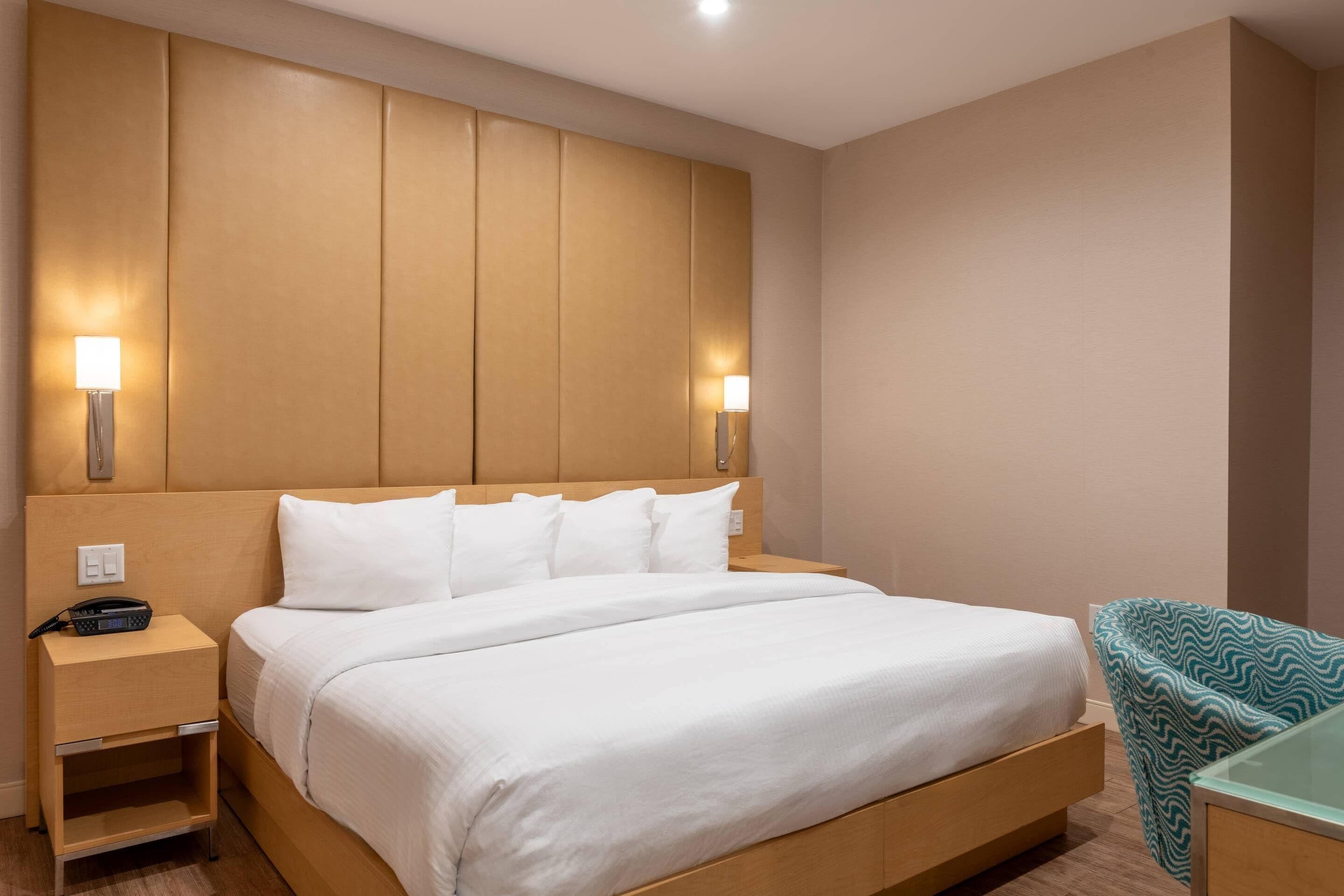 Een hotelkamer met een groot bed, bedlampjes, een nachtkastje en een stoel.