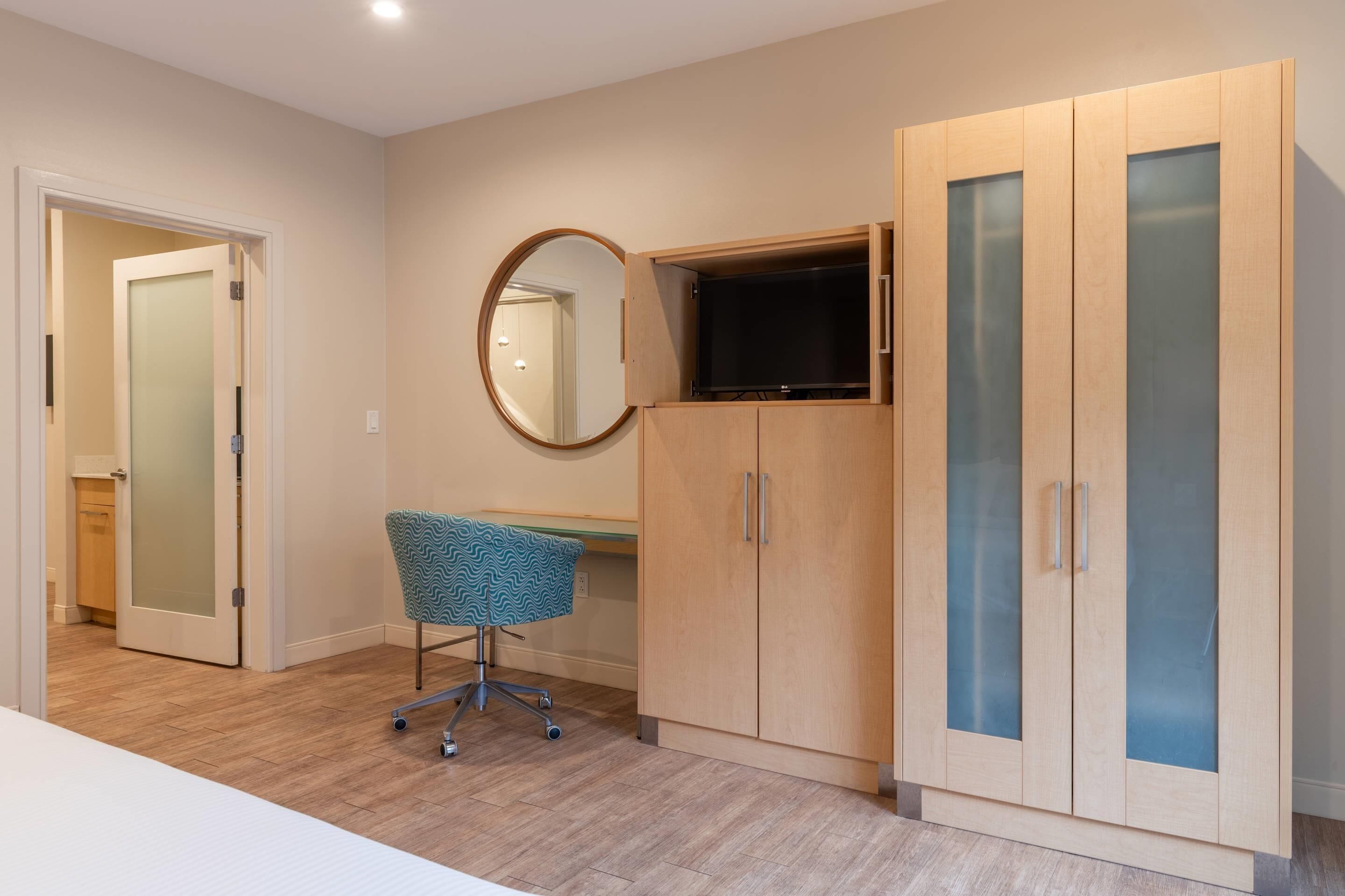 A room with a wooden wardrobe, a desk, and a chair.