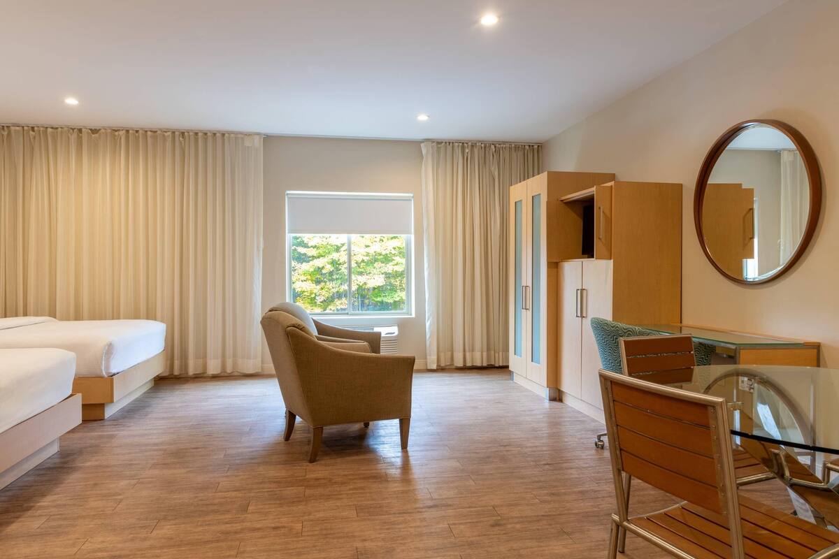 A hotel room with a bed, a chair, a desk with a mirror, and a window with curtains.