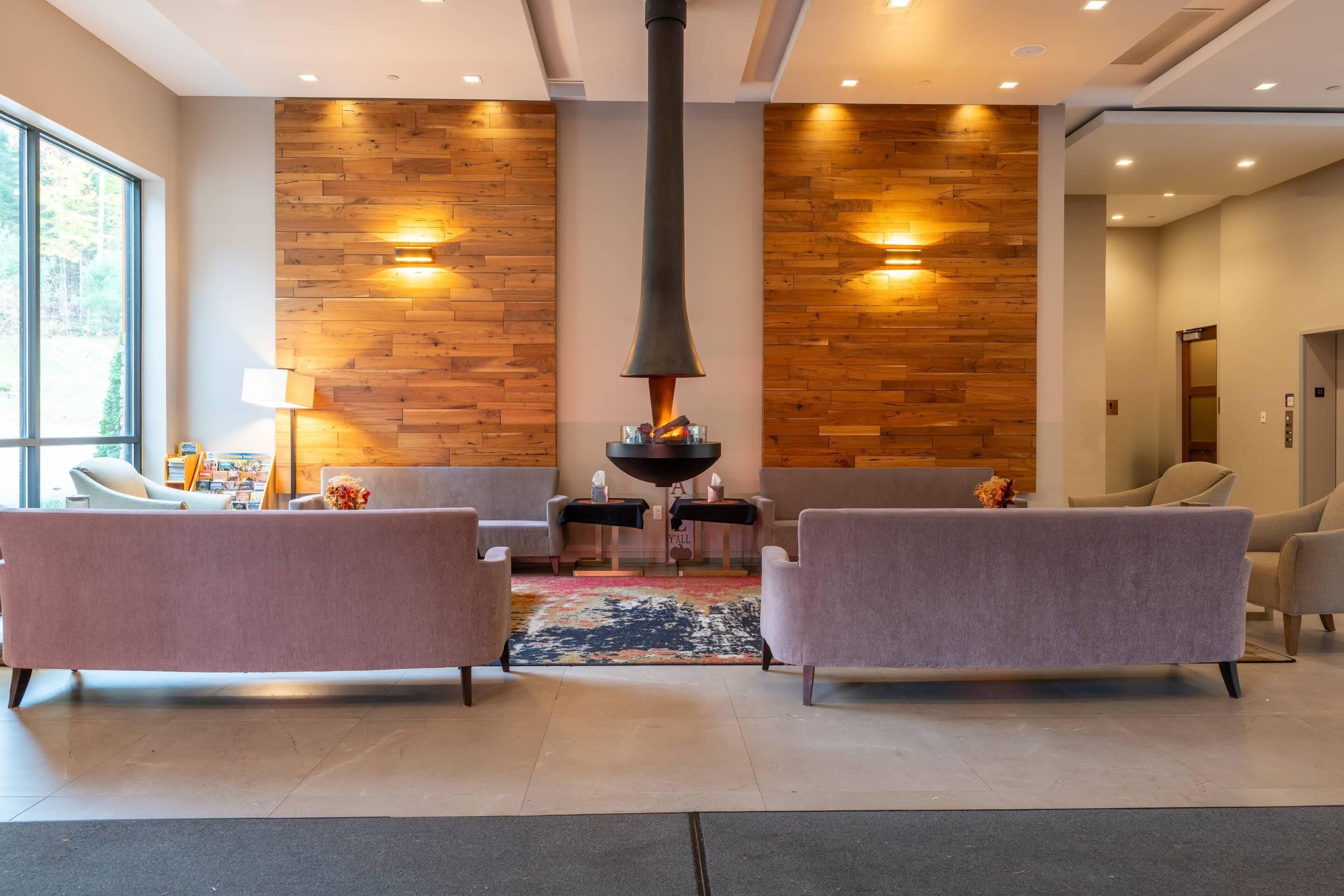 A modern lobby with a wood-paneled wall, a central fireplace, and seating areas.