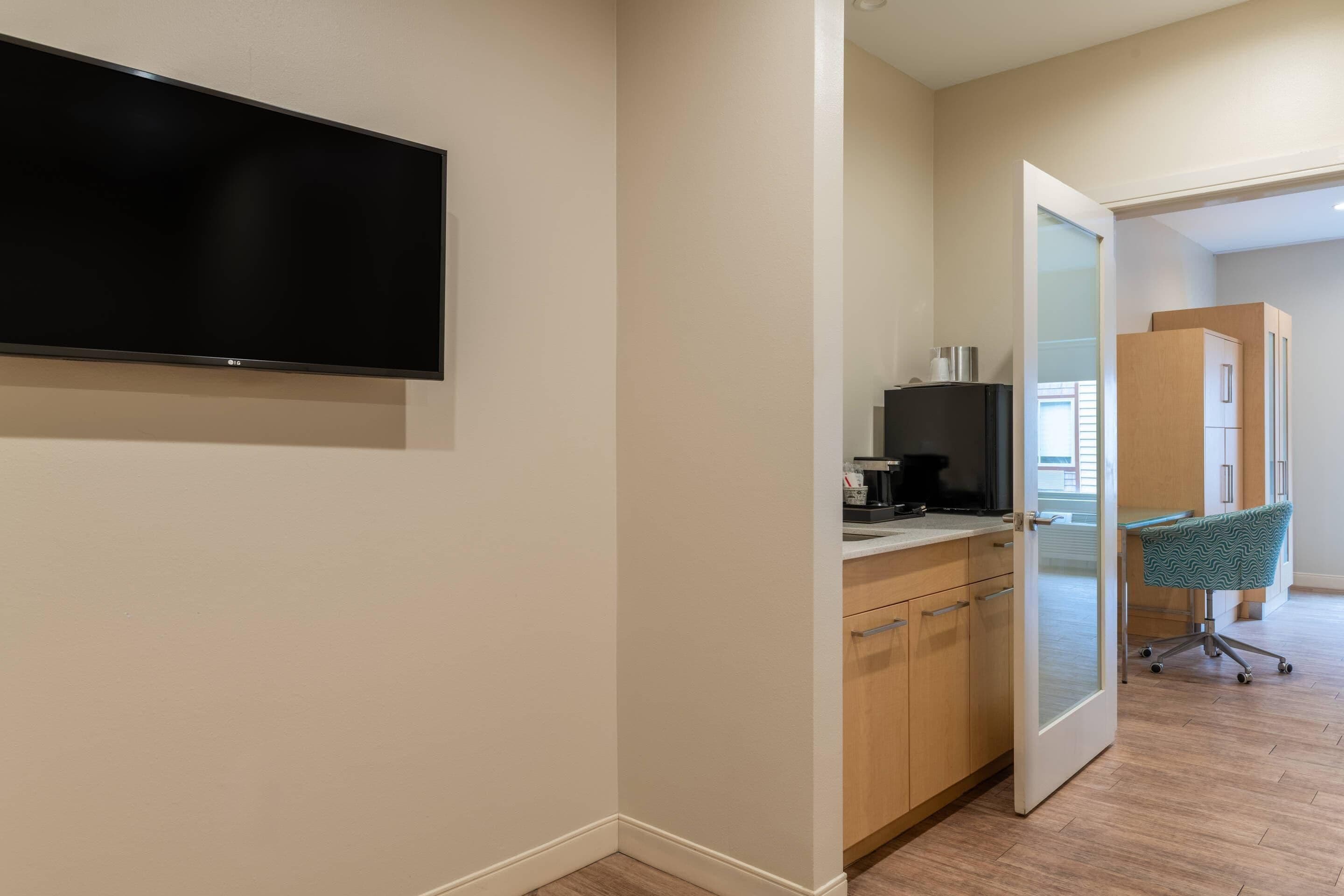 A modern kitchen with a flat-screen TV, wooden cabinets, and a teal office chair.