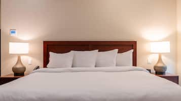 A neatly made bed with a wooden headboard, two bedside lamps, and a wall-mounted thermostat.
