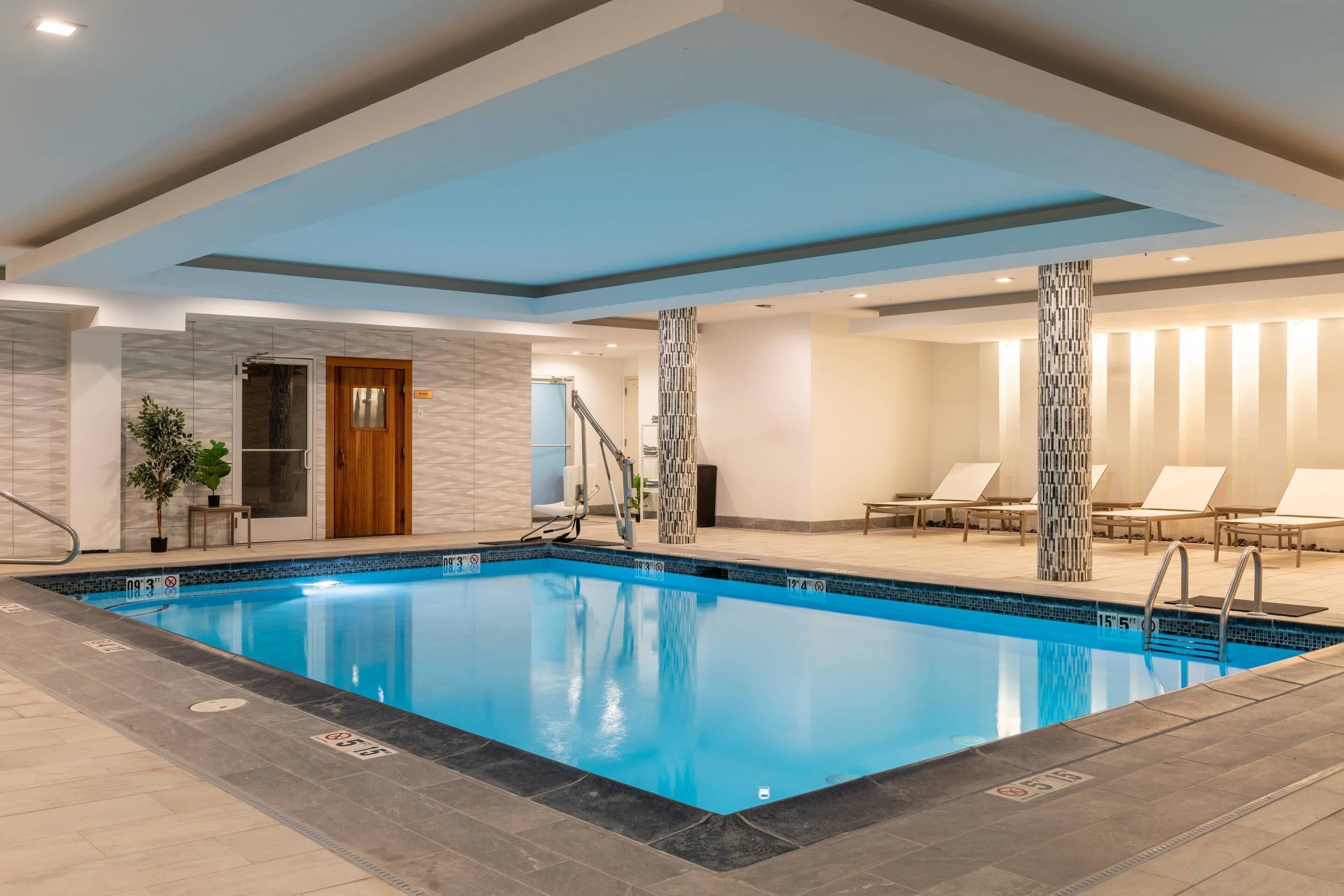 Una piscina interior con agua cristalina, rodeada de sillas de descanso y una escalera que conduce a un nivel superior.