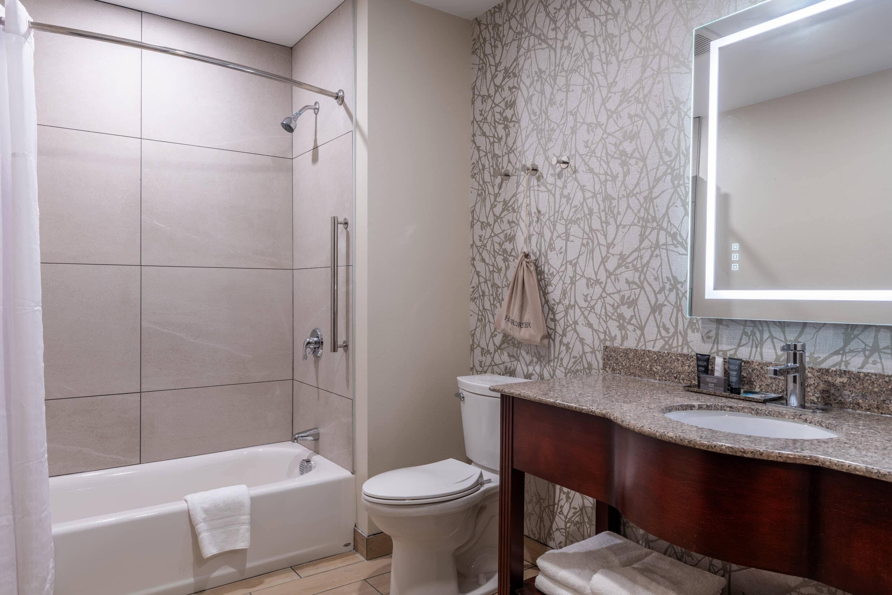 A bathroom with a bathtub, toilet, vanity with sink, and a large mirror.