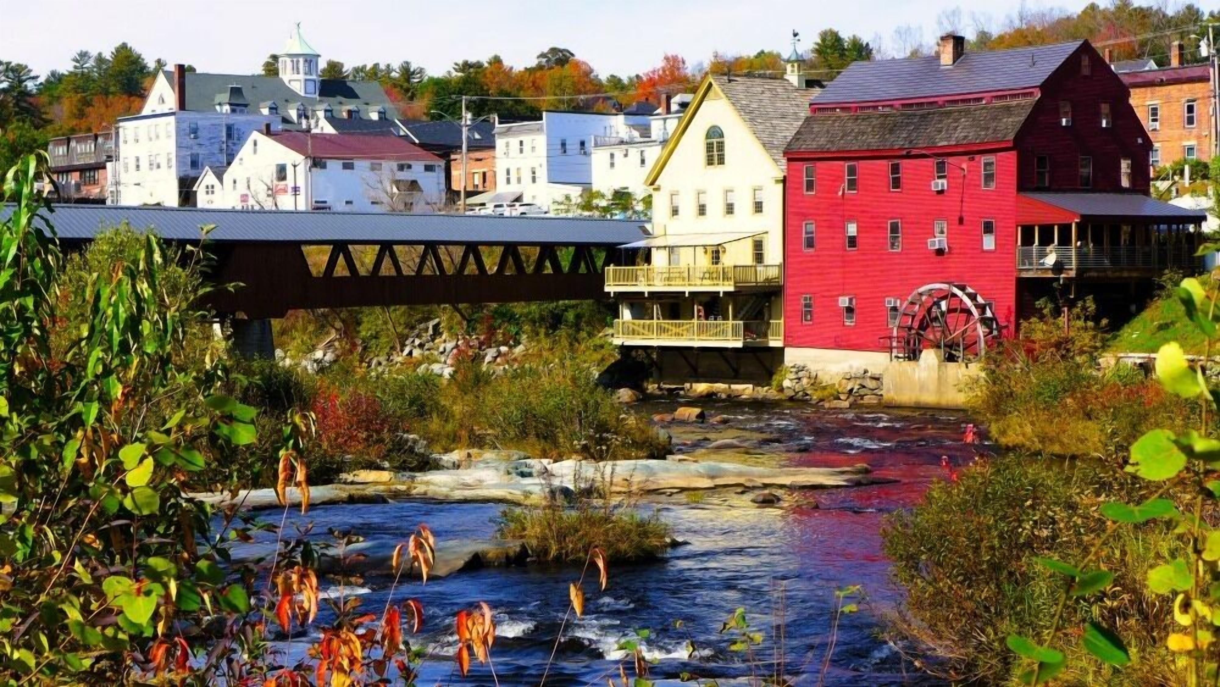 A river with a water wheel and buildings in the background.