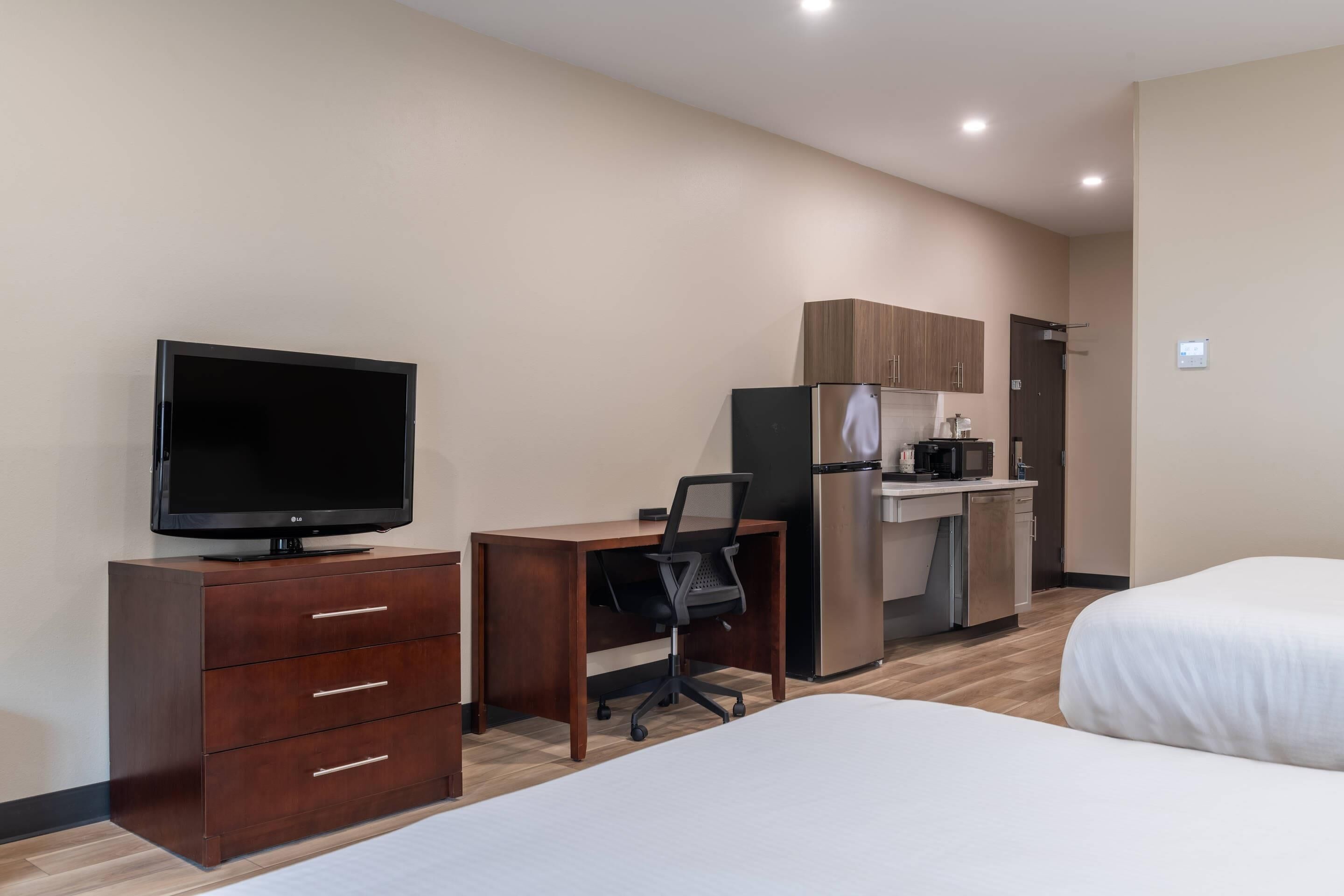 A hotel room with a bed, a desk with a chair, a television, a refrigerator, and a microwave.